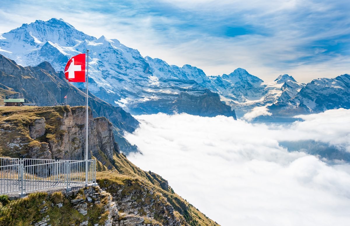 Swiss flag on a mountain ridge above the Alps and a sea of clouds